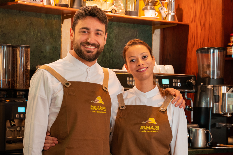 Foto di Fabio, bar Manager della Torrefazione Ernani in divisa dietro al banco, insieme a Monia, assistente.