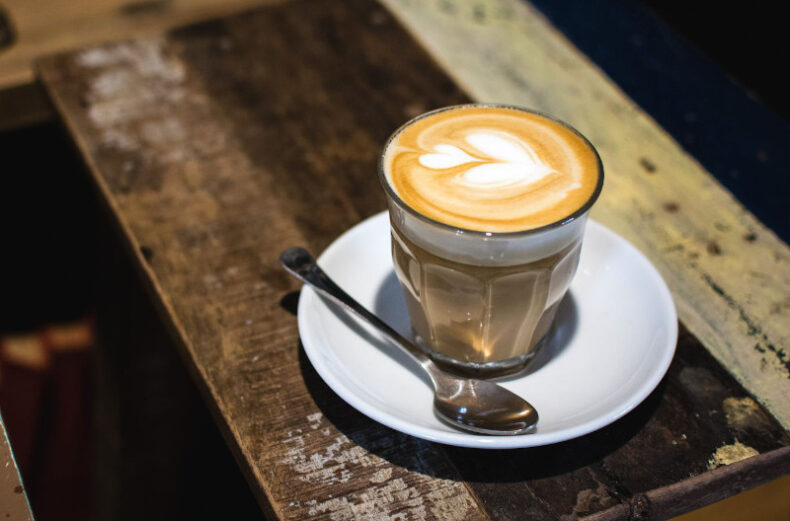 Foto di un tavolo di legno con al centro un cortado in tazza di vetro vintage e decorato con latte art.