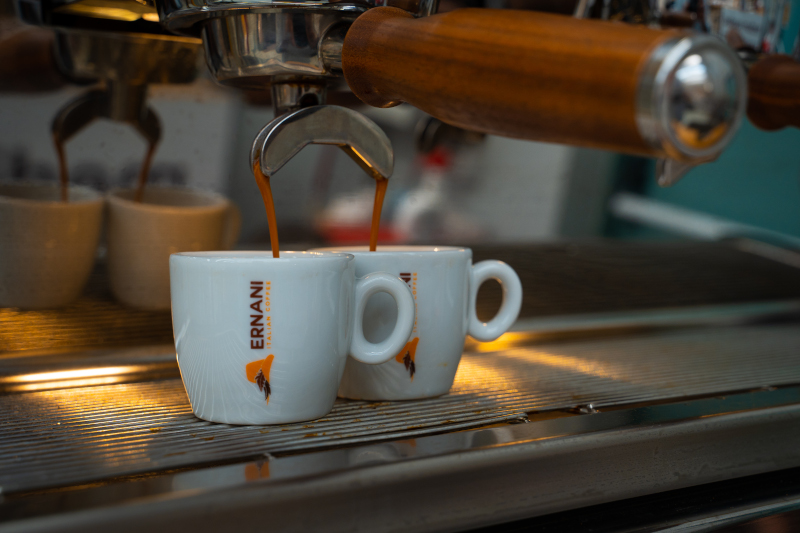 Due tazzie Ernani di porcellana, mentre stanno raccogliendo il caffè estratto dalla macchina da Espresso.