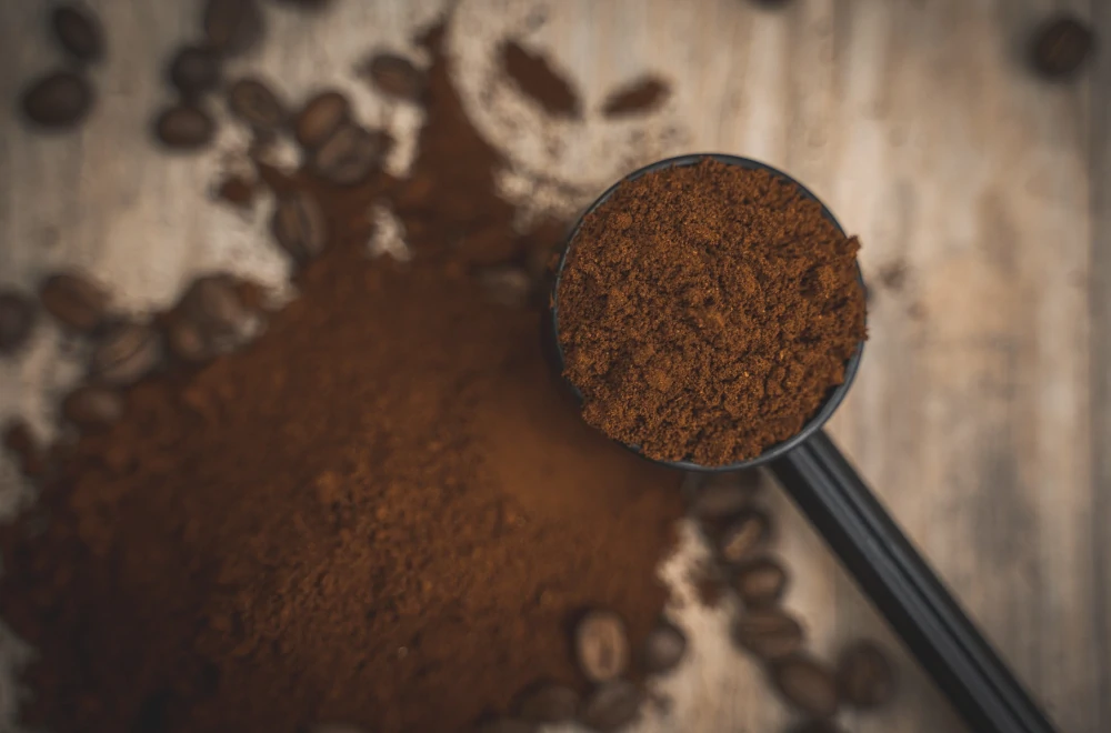 Foto del caffè macinato a tostatura media, di un bel colore marrone caldo, dentro ad un cucchiaio su sfondo in legno.